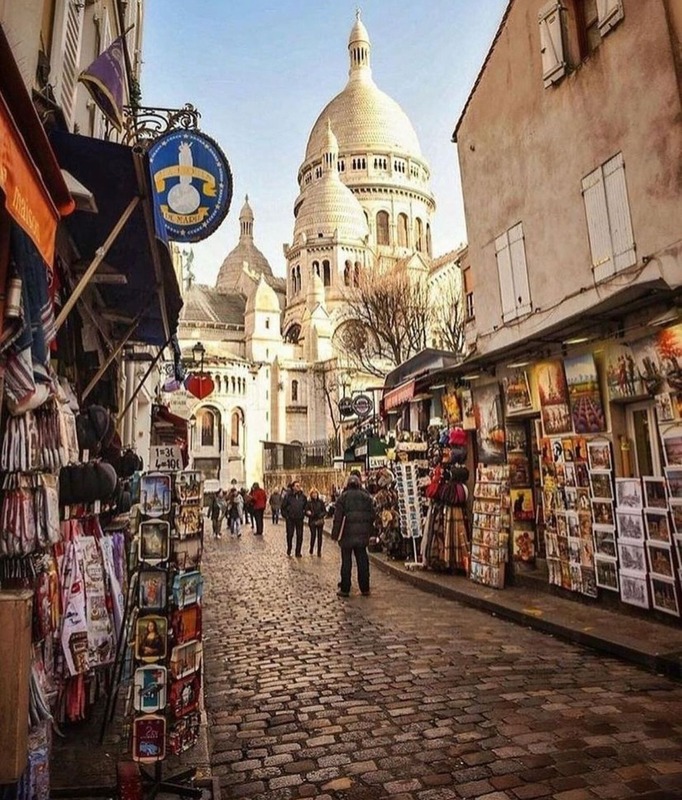 Una calle empedrada de Montmartre con sus tiendas y, al fondo, el Sacré-Cœur